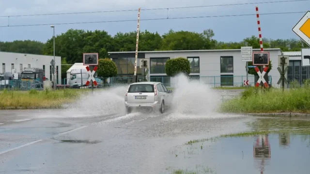 Ein-Auto-faehrt-an-einem-Bahnuebergang-durch-eine-Pfuetze-Nach-der-Sommerhitze-hat-ein-Wetterumschwung-am-Wochenende-in-Teilen-Bayerns-fuer-zahlreiche-witterungsbedingte-Einsaetze-gesorgt